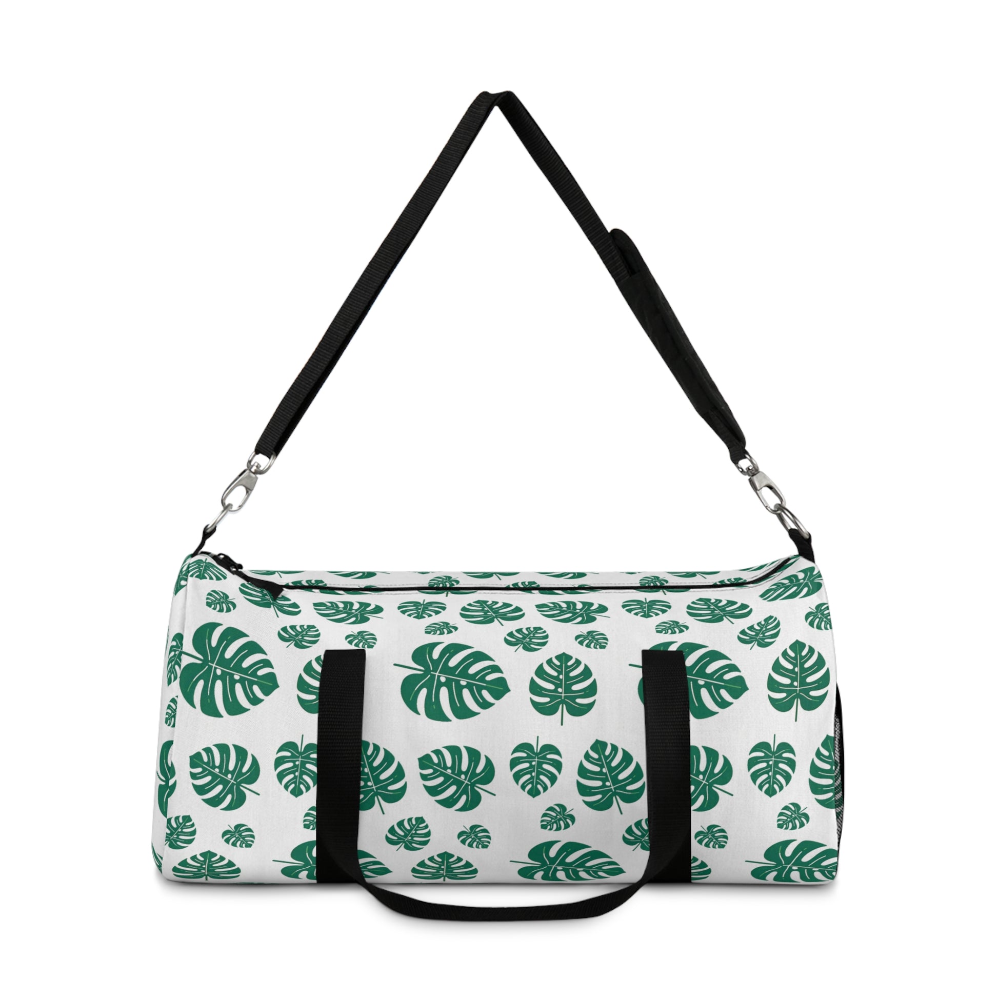 The image shows a cylindrical duffel bag patterned with green tropical leaves and equipped with a black shoulder strap