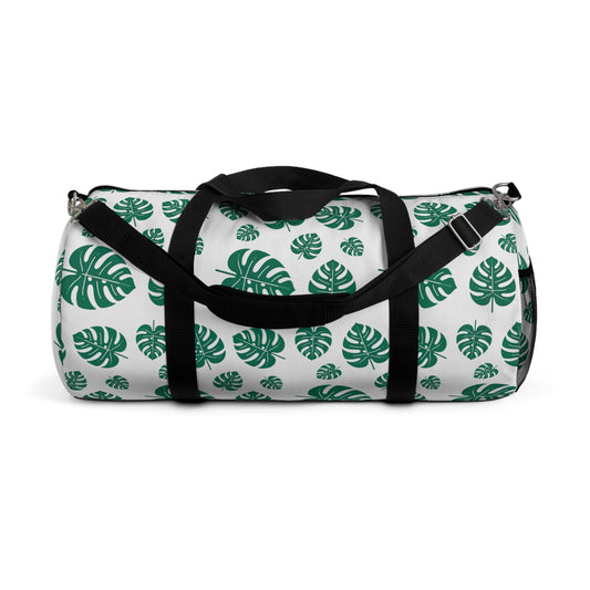 The image shows a cylindrical duffel bag patterned with green tropical leaves and equipped with a black shoulder strap