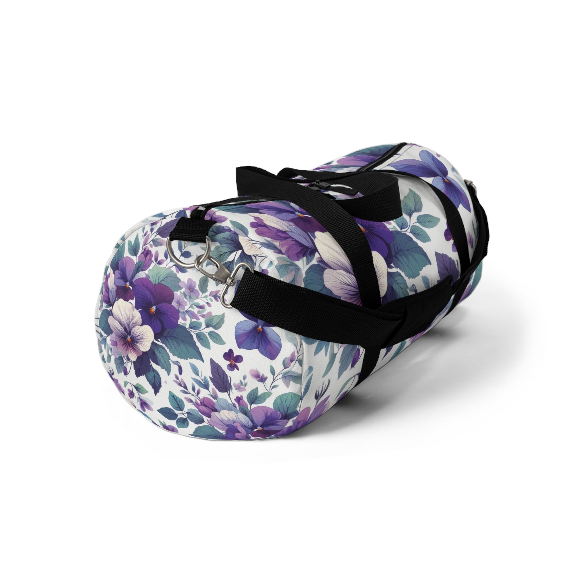 The image shows a cylindrical duffel bag with a floral pattern, featuring a variety of purple flowers and green leaves, complete with black straps for carrying