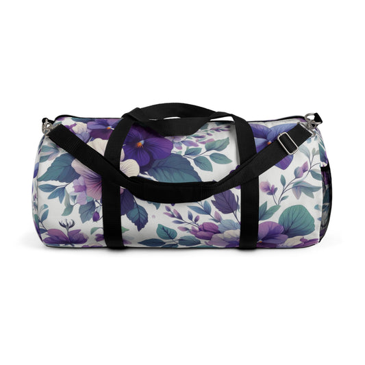 The image shows a cylindrical duffel bag with a floral pattern, featuring a variety of purple flowers and green leaves, complete with black straps for carrying