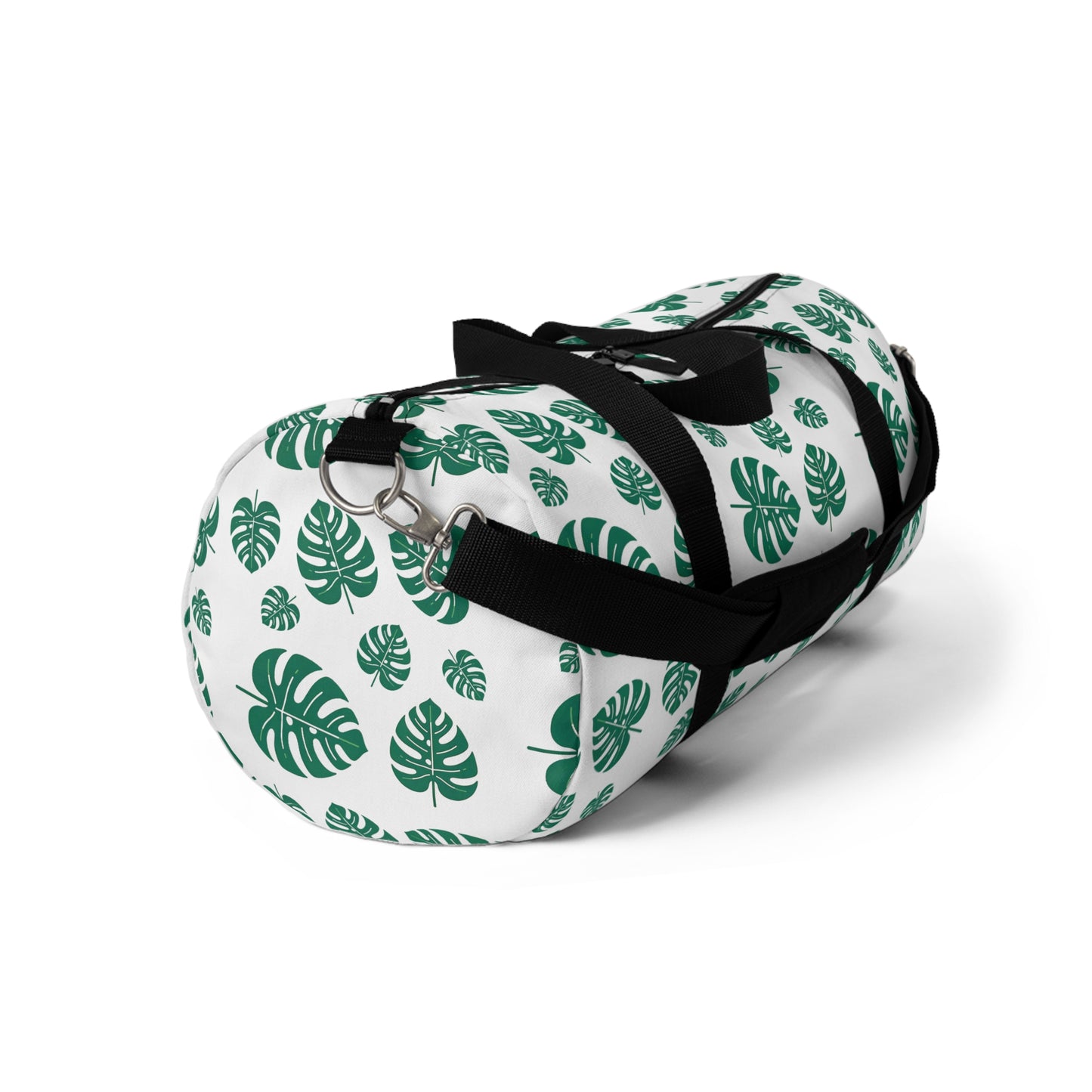 The image shows a cylindrical duffel bag patterned with green tropical leaves and equipped with a black shoulder strap